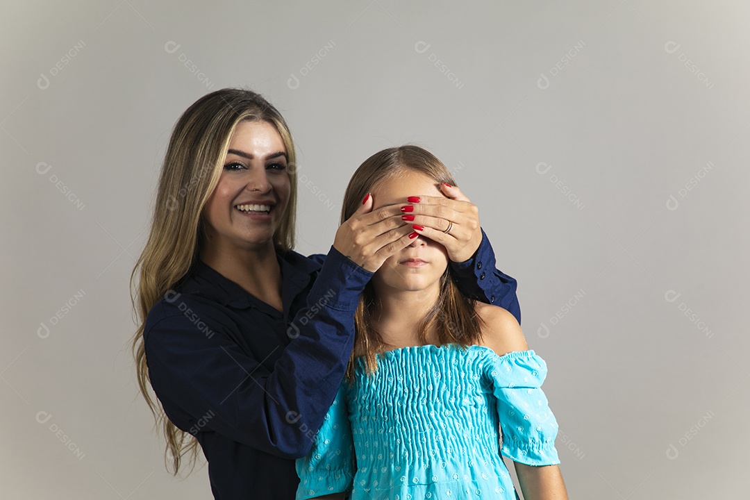 Linda mulher sorridente tampando olho de menina com as mãos sobre fundo isolado