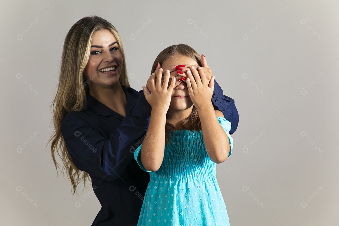 Linda mulher sorridente tampando olho de menina com as mãos sobre fundo isolado