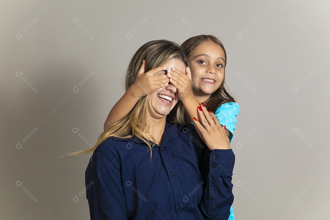 Linda criança sorridente tampando olho de uma mulher com as mãos sobre fundo isolado