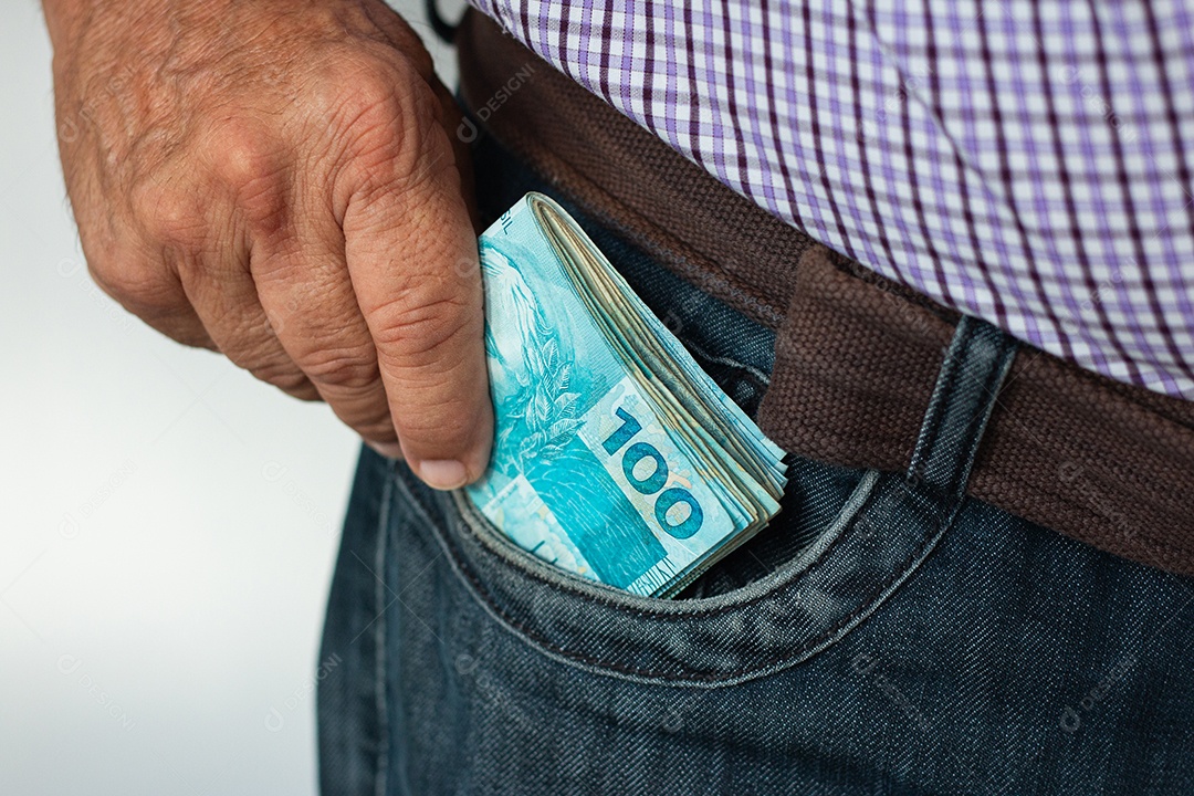 Homem colocando um maço de notas de 100 reais no bolso da calça jeans