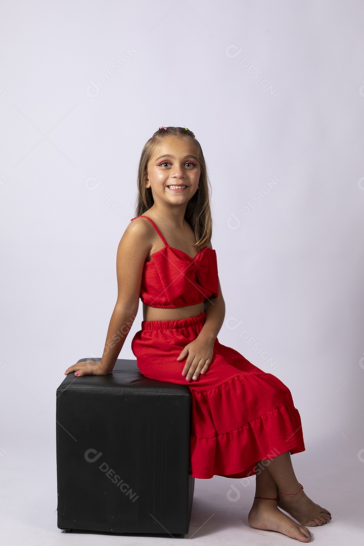 Linda menina sentada com look vermelho sobre fundo de studio isolado