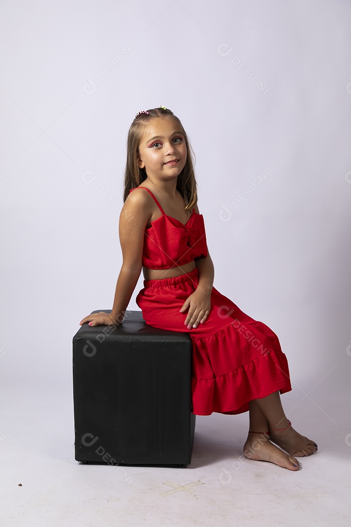 Linda menina sentada com look vermelho sobre fundo de studio isolado