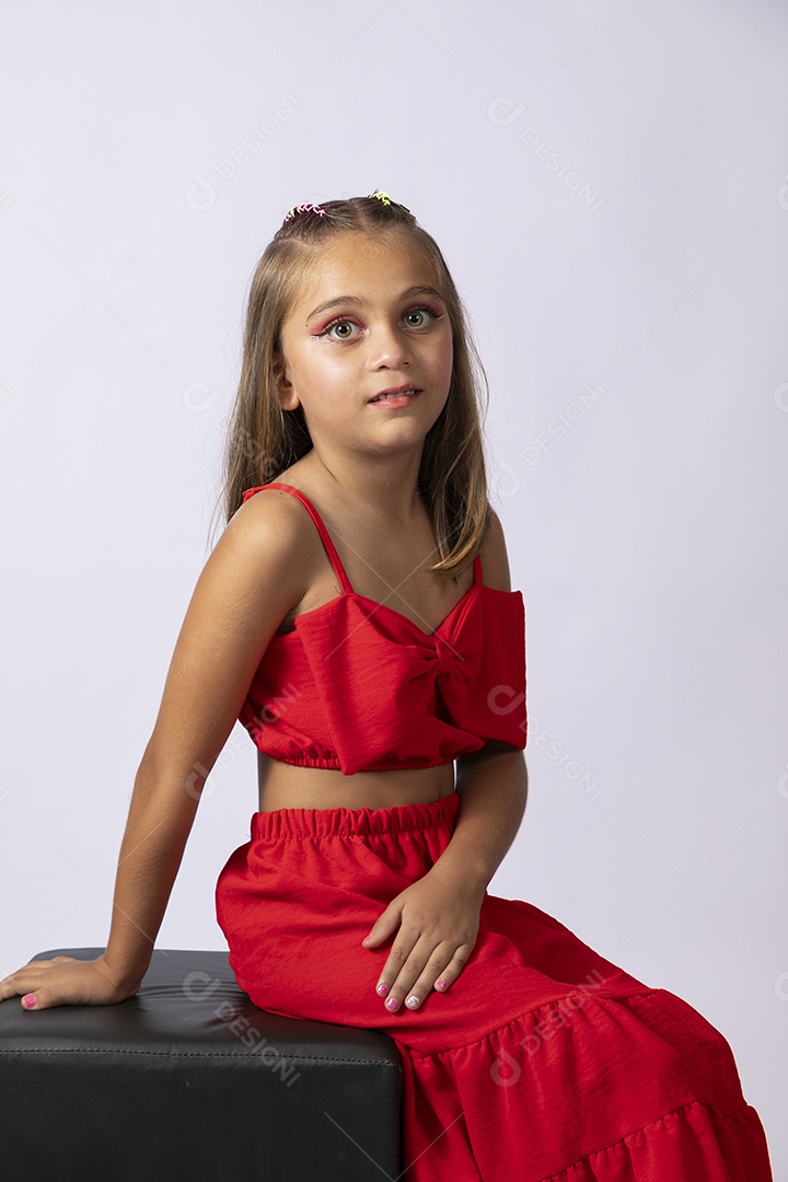 Linda menina sentada com look vermelho sobre fundo de studio isolado
