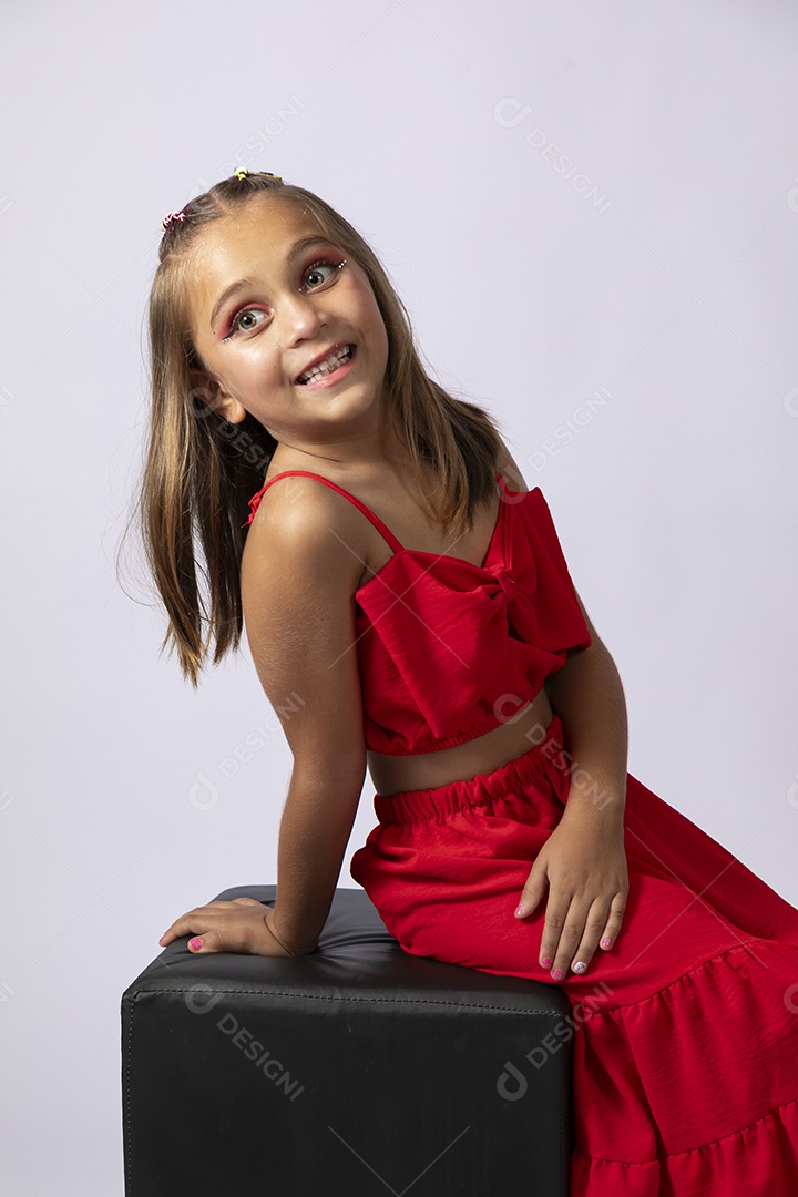 Linda menina sentada com look vermelho sobre fundo de studio isolado
