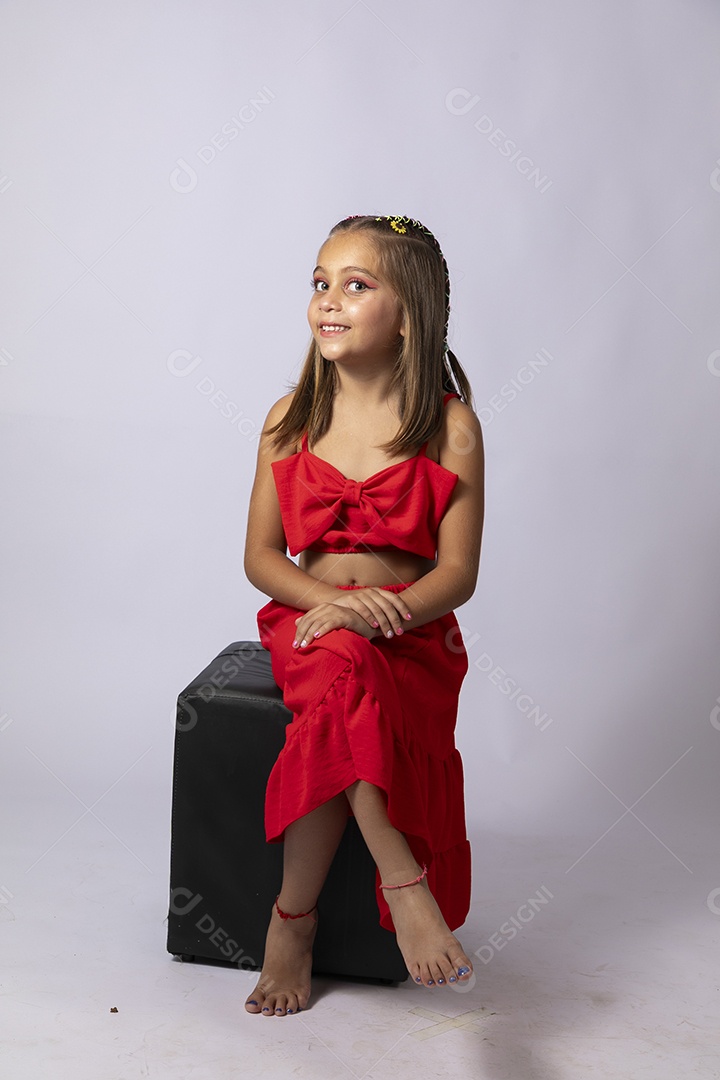 Linda menina sentada com look vermelho sobre fundo de studio isolado
