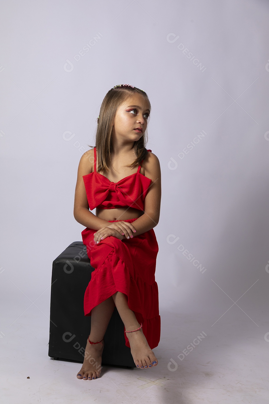 Linda menina sentada com look vermelho sobre fundo de studio isolado