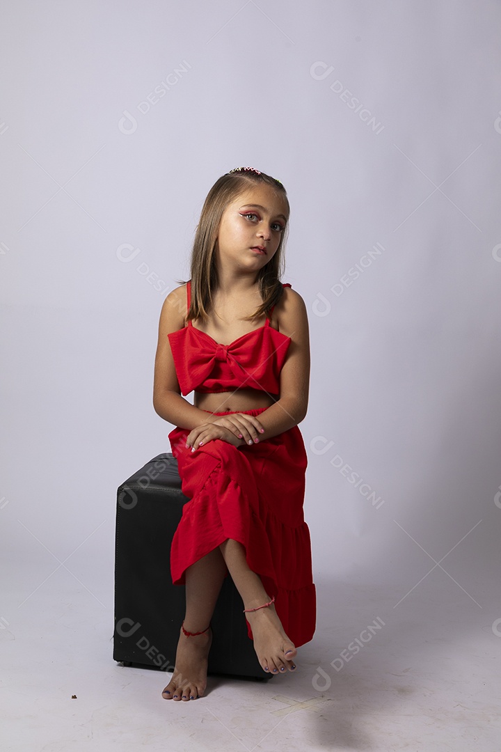 Linda menina sentada com look vermelho sobre fundo de studio isolado