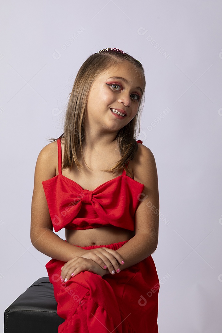 Linda menina sentada com look vermelho sobre fundo de studio isolado