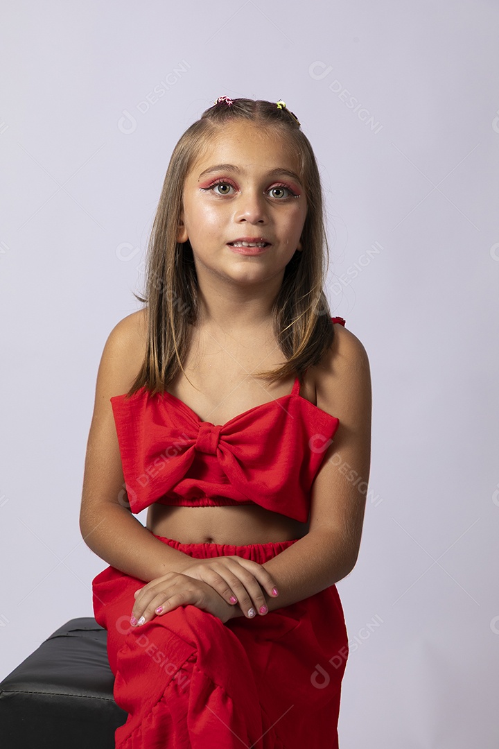 Linda menina sentada com look vermelho sobre fundo de studio isolado