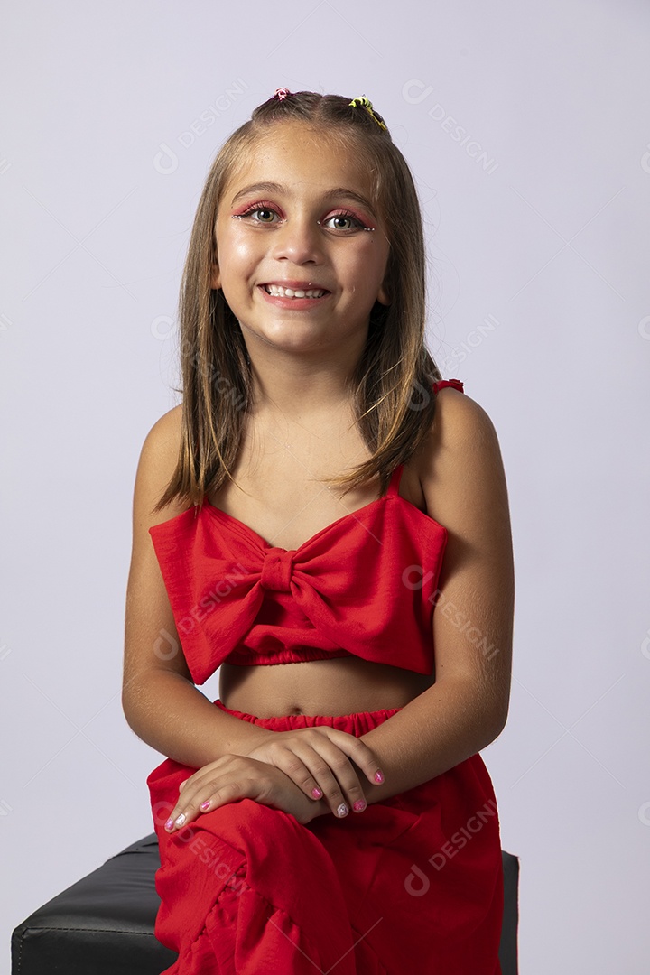 Linda menina sentada com look vermelho sobre fundo de studio isolado