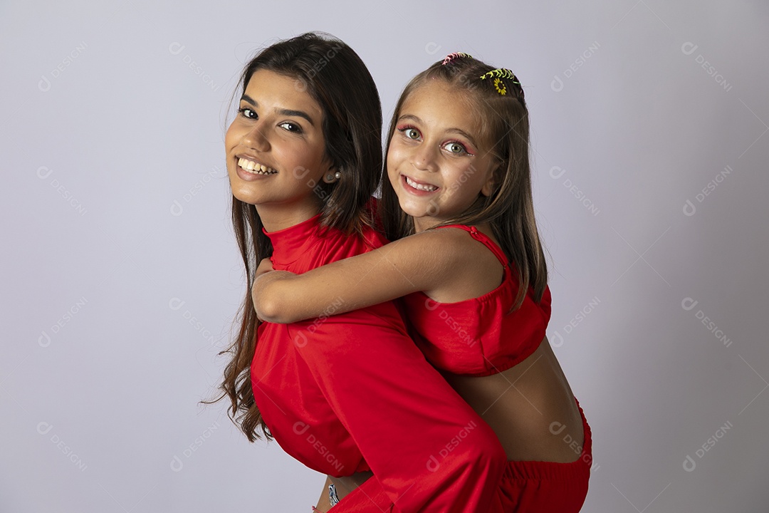 Linda mãe segurando garotinha nas costa com looks vermelhos sobre studio isolado