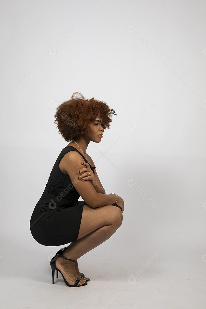 Linda mulher negra de cabelo cacheados agachada sobre fundo branco isolado