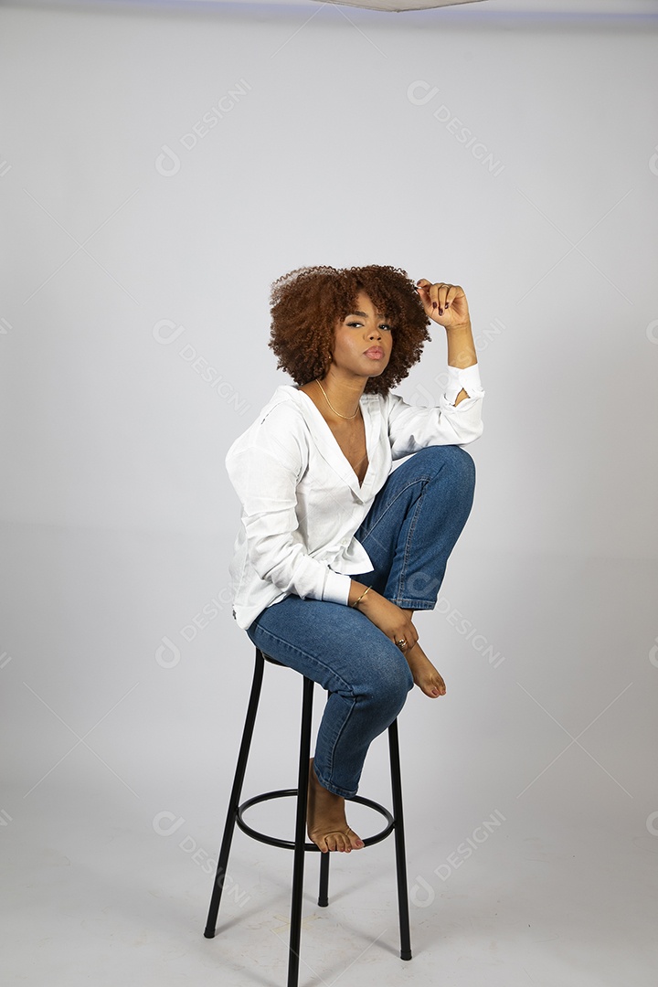 Linda mulher negra de cabelo cacheados sentada fazendo pose sobre fundo branco isolado