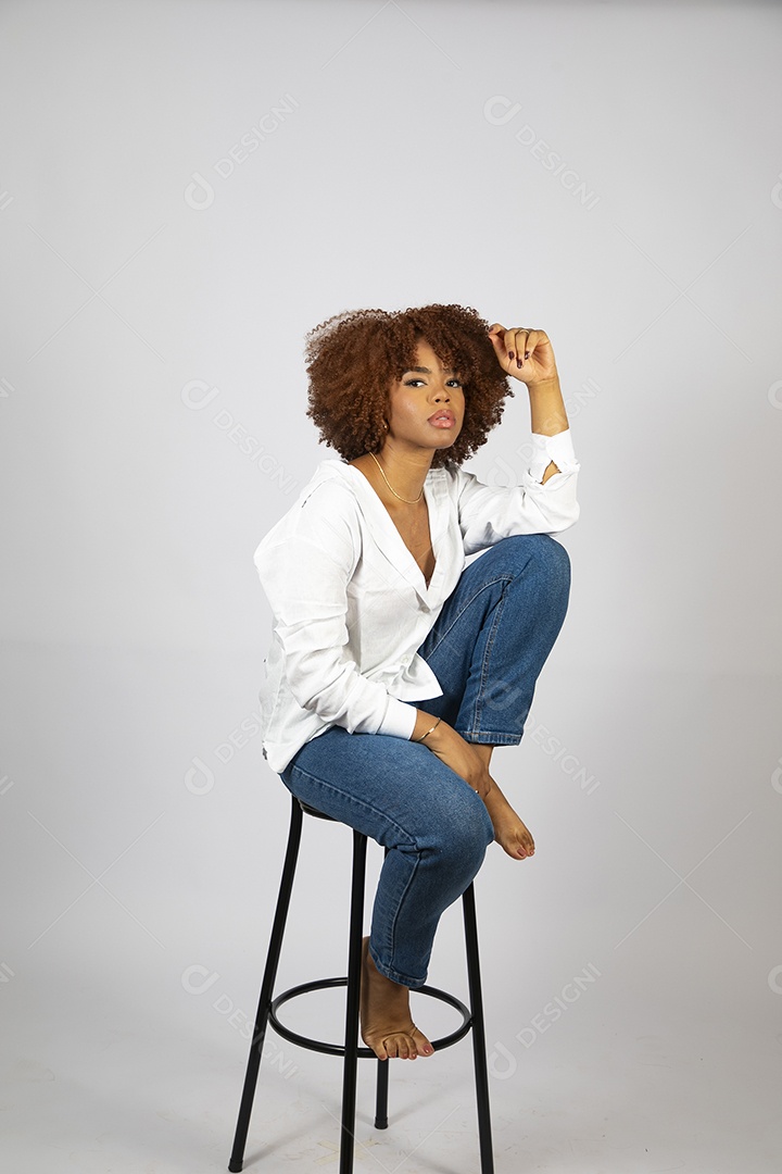 Linda mulher negra de cabelo cacheados sentada fazendo pose sobre fundo branco isolado