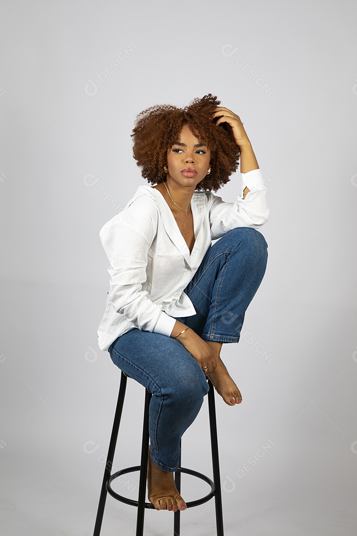 Linda mulher negra de cabelo cacheados sentada fazendo pose sobre fundo branco isolado