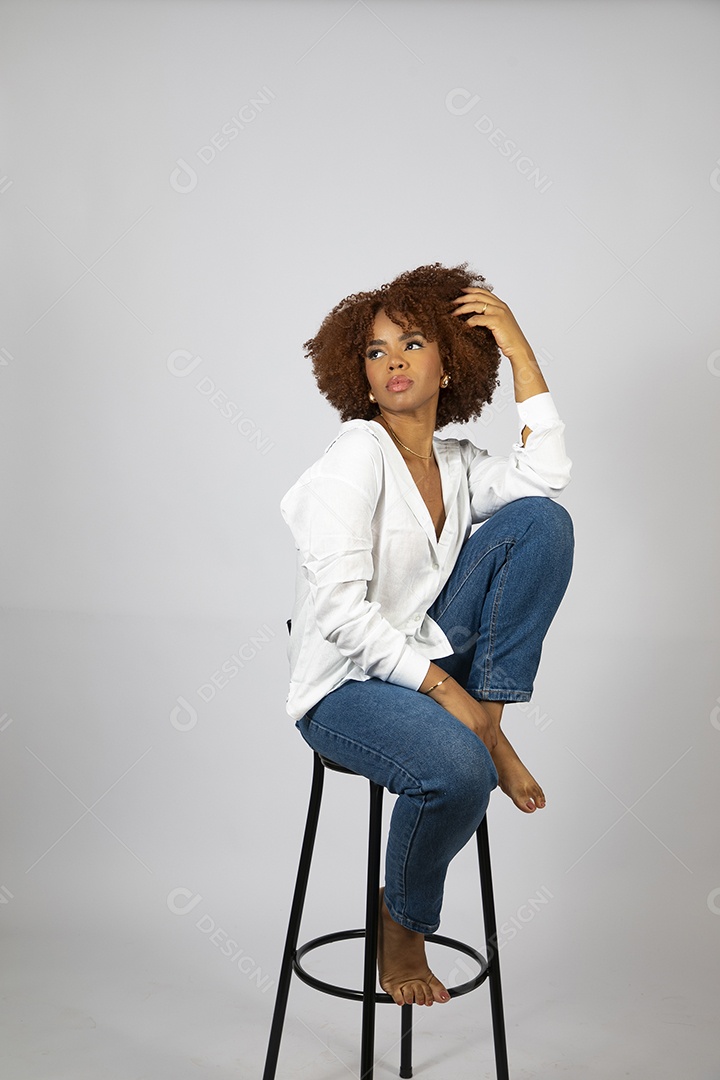 Linda mulher negra de cabelo cacheados sentada fazendo pose sobre fundo branco isolado