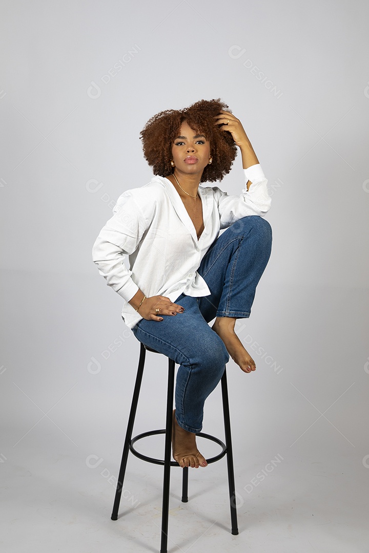 Linda mulher negra de cabelo cacheados sentada fazendo pose sobre fundo branco isolado