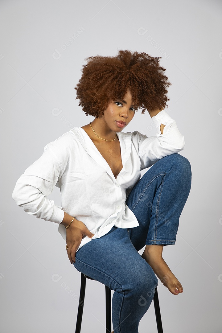Linda mulher negra de cabelo cacheados sentada fazendo pose sobre fundo branco isolado