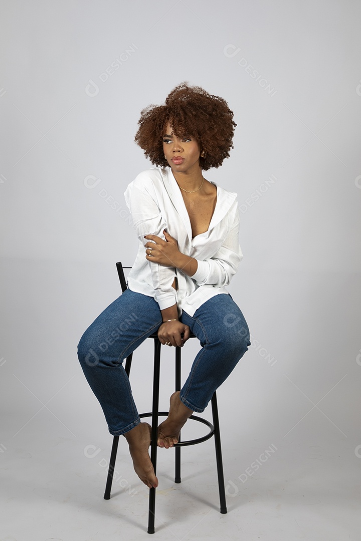 Linda mulher negra de cabelo cacheados sentada fazendo pose sobre fundo branco isolado