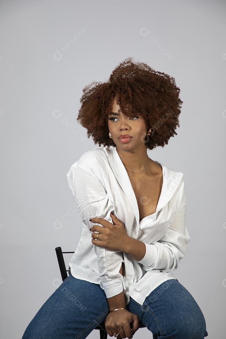 Linda mulher negra de cabelo cacheados sentada fazendo pose sobre fundo branco isolado