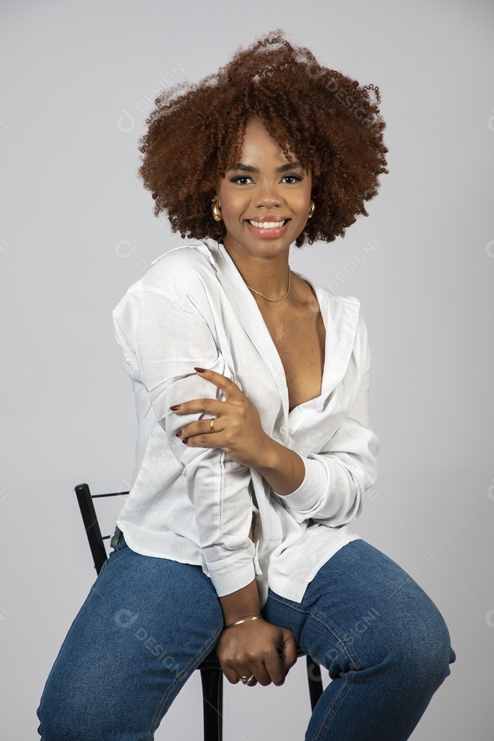 Linda mulher negra de cabelo cacheados sentada fazendo pose sobre fundo branco isolado