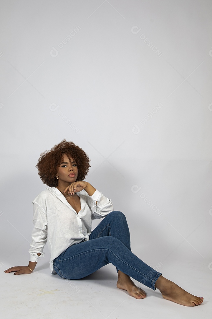 Linda mulher negra de cabelo cacheados sentada fazendo pose sobre fundo branco isolado