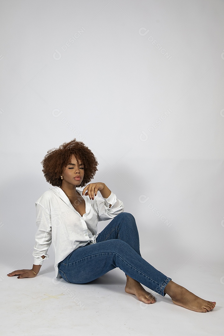 Linda mulher negra de cabelo cacheados sentada fazendo pose sobre fundo branco isolado