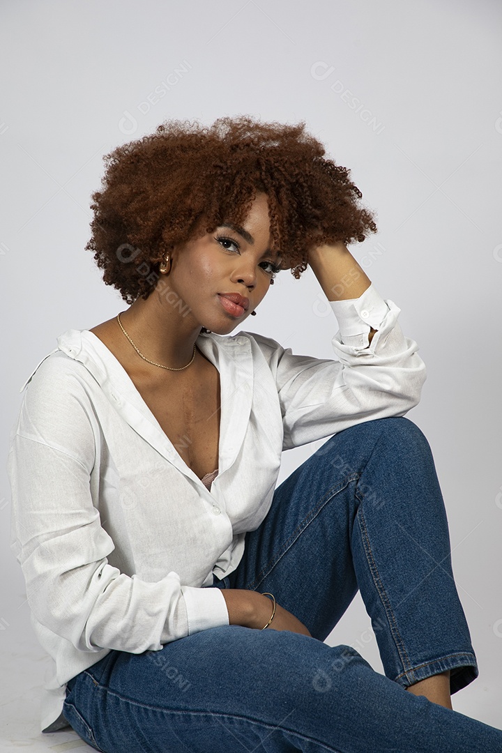 Linda mulher negra de cabelo cacheados sentada fazendo pose sobre fundo branco isolado