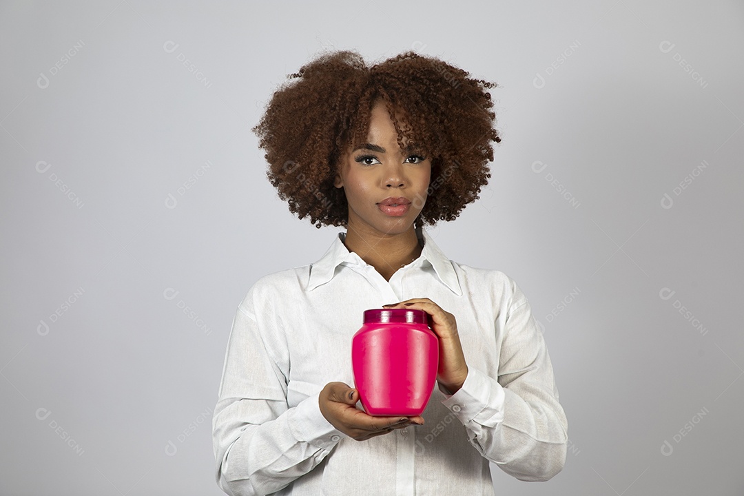 Linda mulher negra de cabelo cacheados segurando pote de creme sobre fundo branco isolado