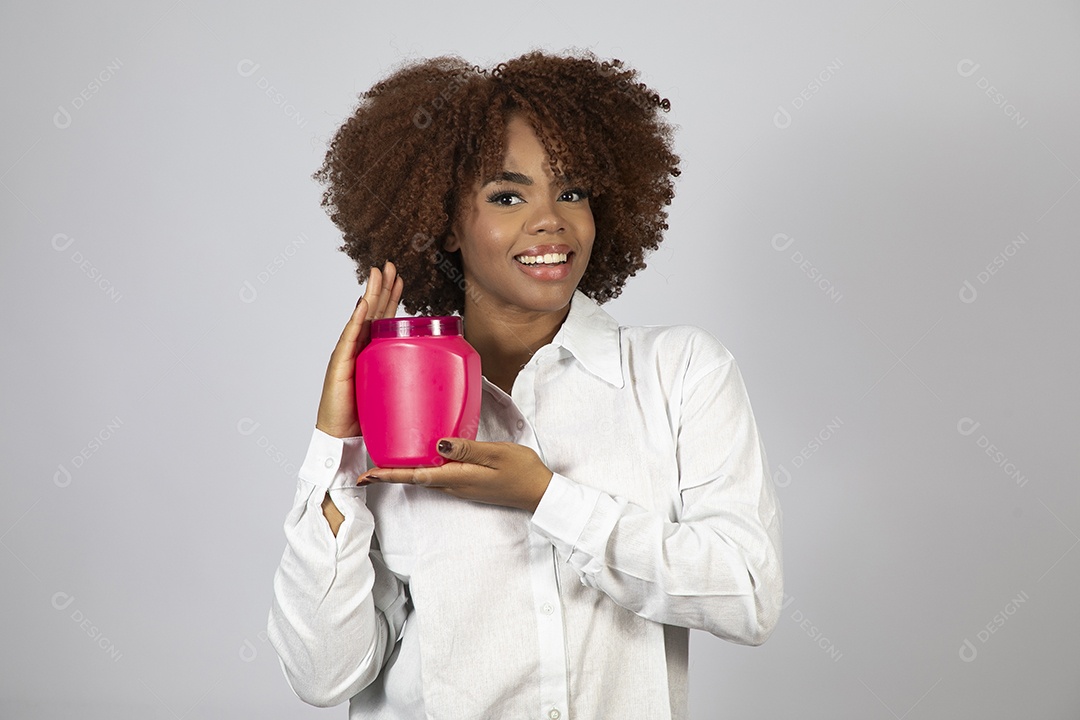 Linda mulher negra de cabelo cacheados segurando pote de creme sobre fundo branco isolado