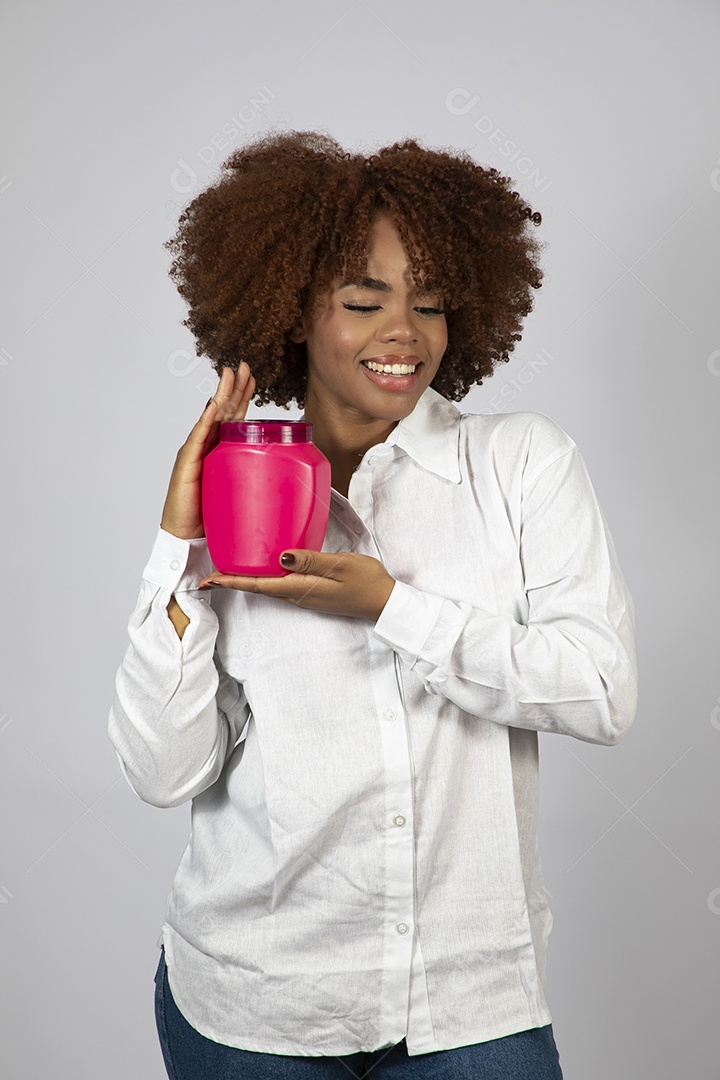 Linda mulher negra de cabelo cacheados segurando pote de creme sobre fundo branco isolado