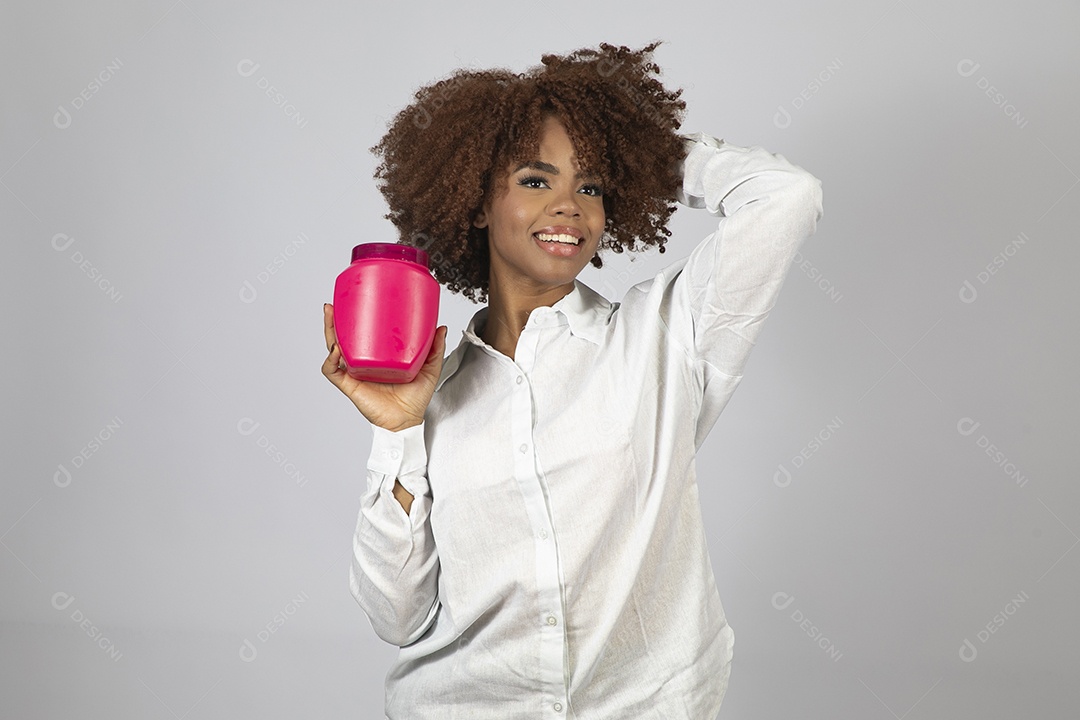 Linda mulher negra de cabelo cacheados segurando pote de creme sobre fundo branco isolado