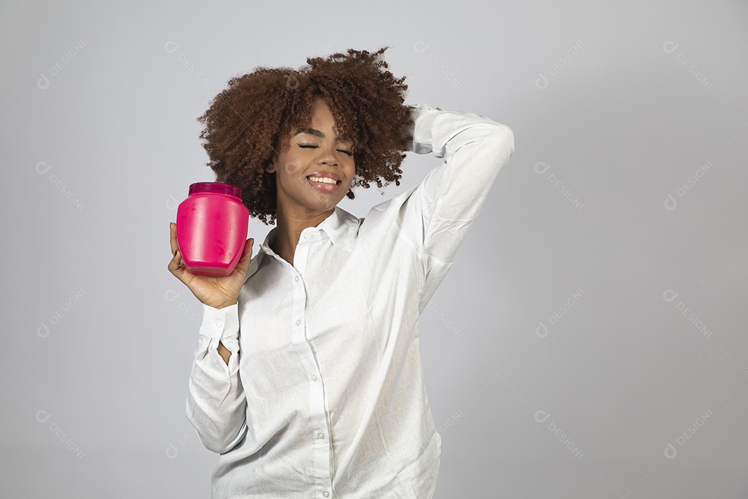 Linda mulher negra de cabelo cacheados segurando pote de creme sobre fundo branco isolado