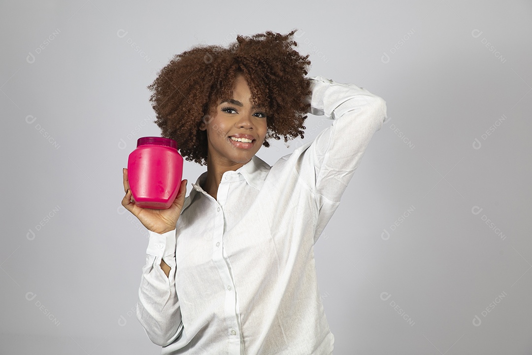 Linda mulher negra de cabelo cacheados segurando pote de creme sobre fundo branco isolado