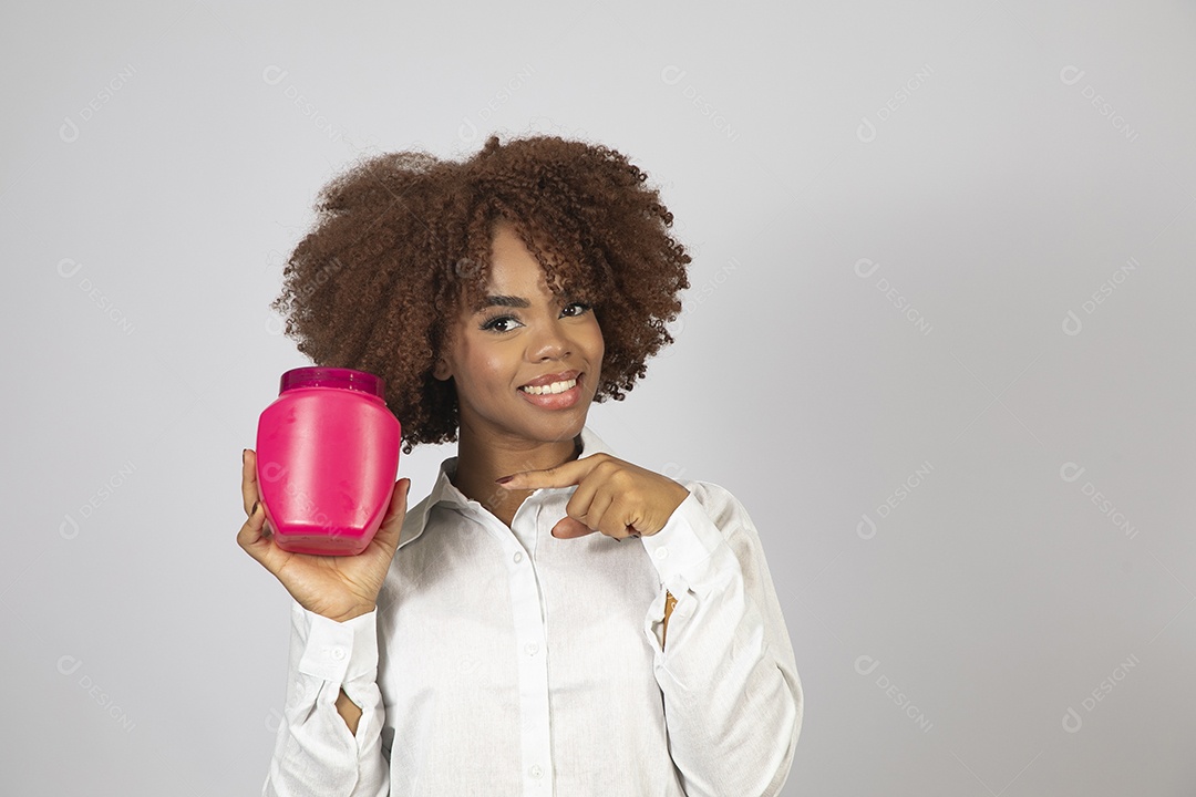 Linda mulher negra de cabelo cacheados segurando pote de creme sobre fundo branco isolado