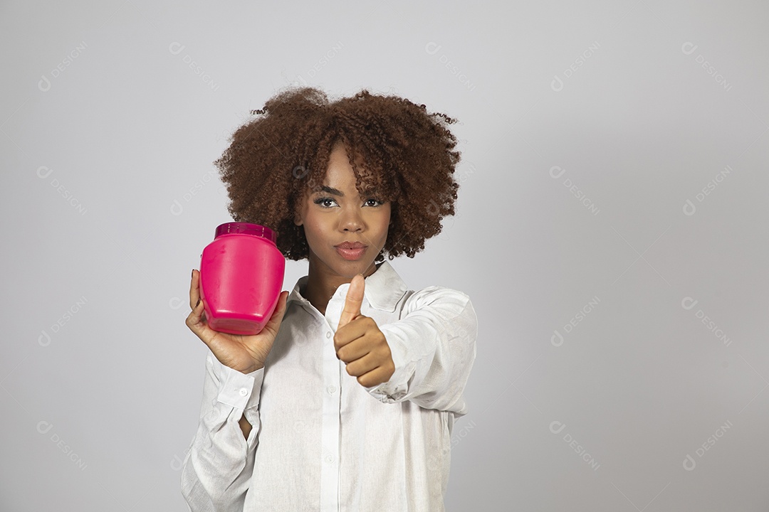 Linda mulher negra de cabelo cacheados segurando pote de creme sobre fundo branco isolado
