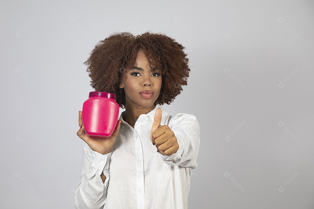 Linda mulher negra de cabelo cacheados segurando pote de creme sobre fundo branco isolado