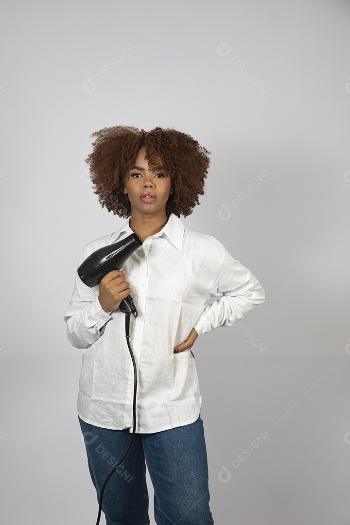 Linda mulher negra de cabelo cacheados segurando secador de cabelo sobre fundo branco isolado
