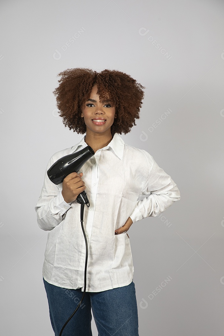 Linda mulher negra de cabelo cacheados segurando secador de cabelo sobre fundo branco isolado