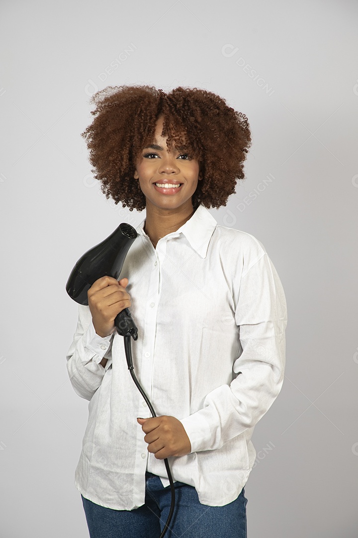 Linda mulher negra de cabelo cacheados segurando secador de cabelo sobre fundo branco isolado