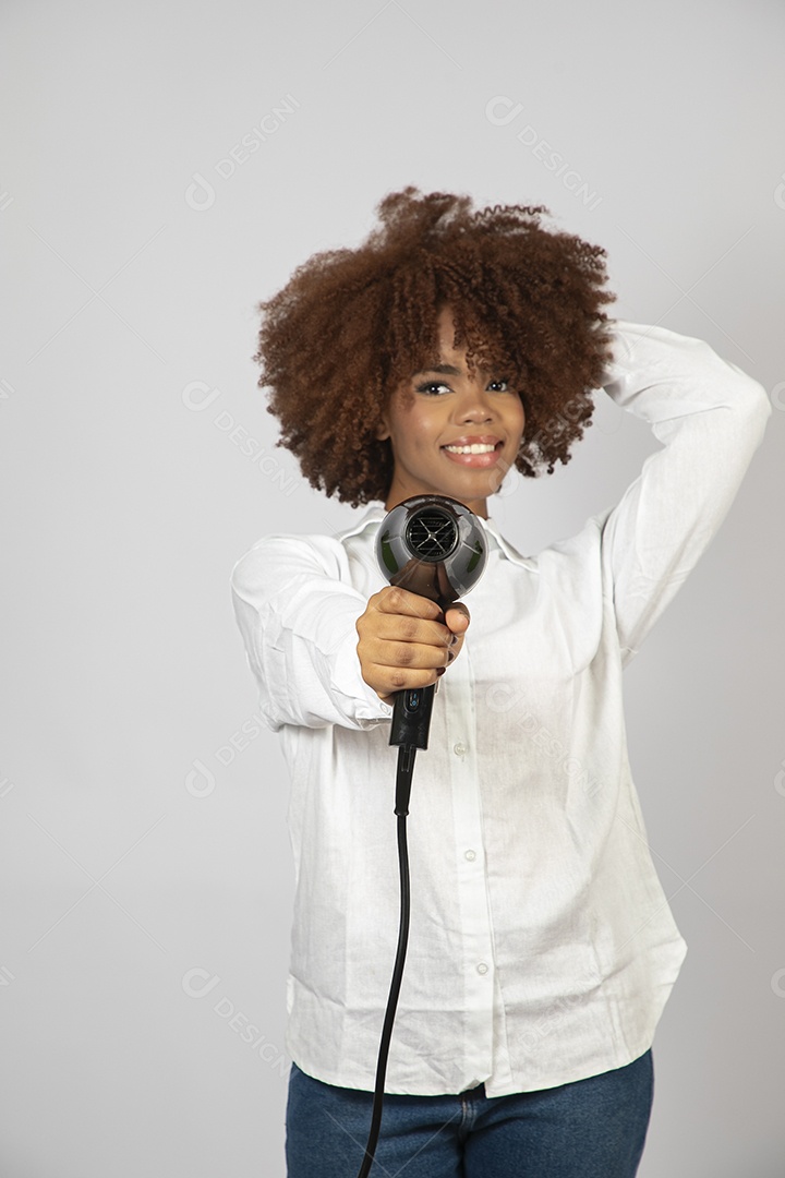 Linda mulher negra de cabelo cacheados segurando secador de cabelo sobre fundo branco isolado