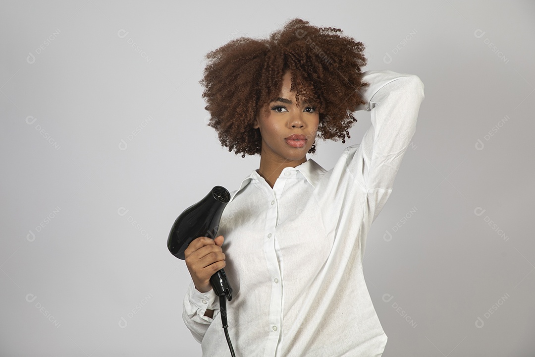 Linda mulher negra de cabelo cacheados segurando secador de cabelo sobre fundo branco isolado