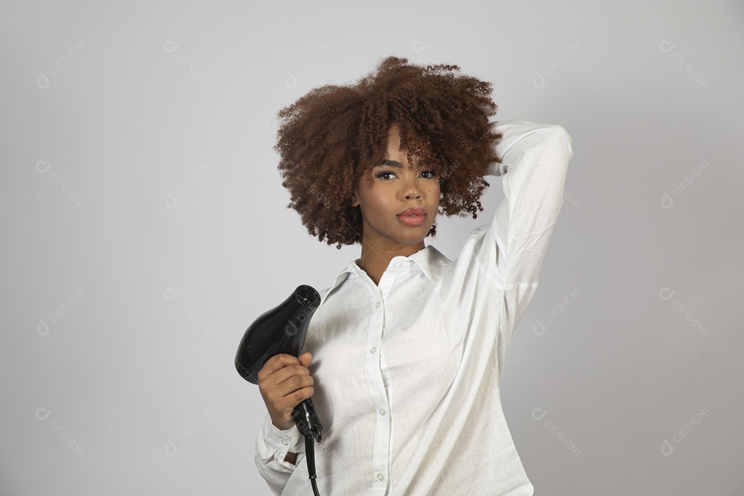 Linda mulher negra de cabelo cacheados segurando secador de cabelo sobre fundo branco isolado