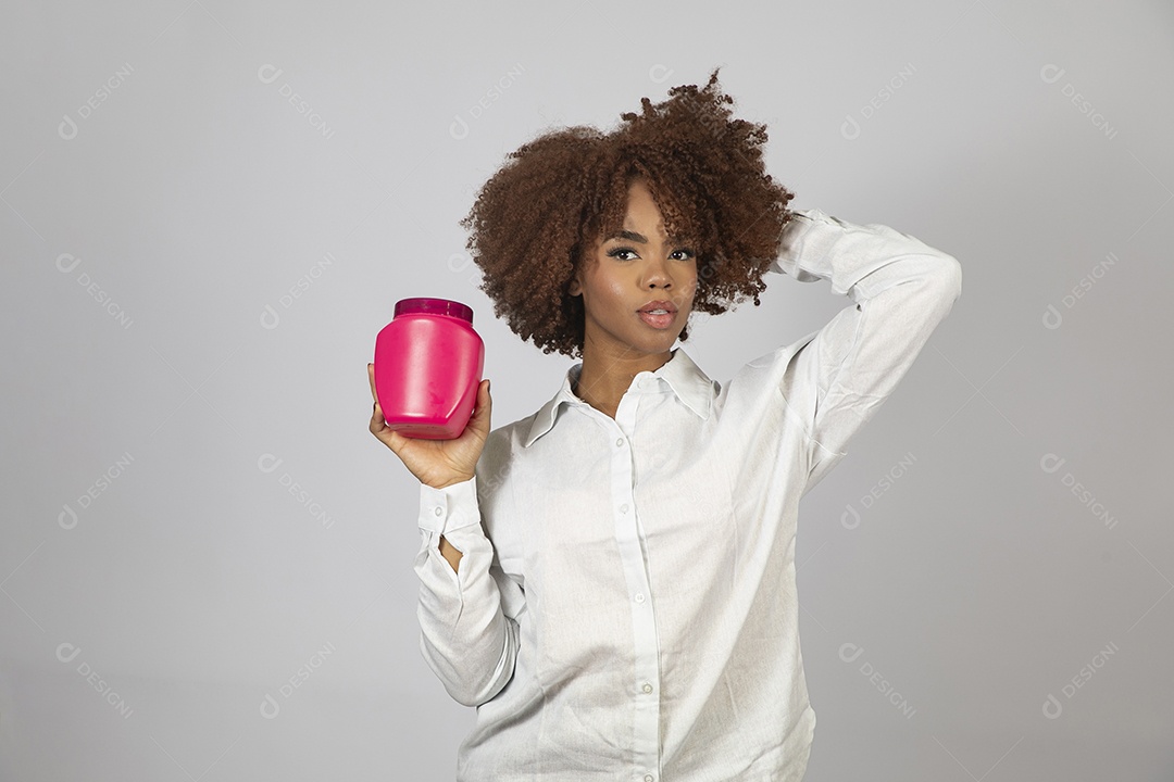 Linda mulher negra de cabelo cacheados segurando pote de creme sobre fundo branco isolado