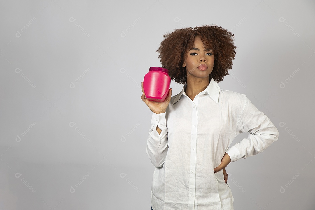 Linda mulher negra de cabelo cacheados segurando pote de creme sobre fundo branco isolado