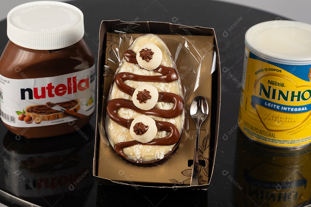 Ovo de páscoa de colher ao lado de leite ninho e nutella sobre uma mesa