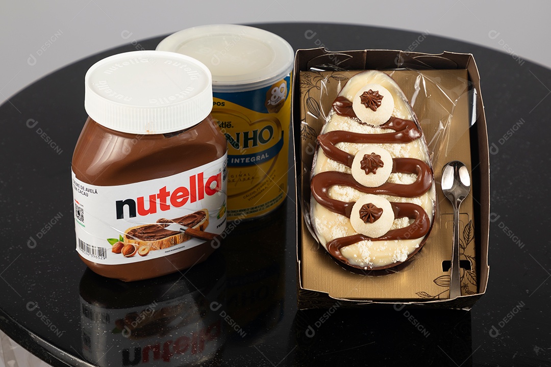 Ovo de páscoa de colher ao lado de leite ninho e nutella sobre uma mesa
