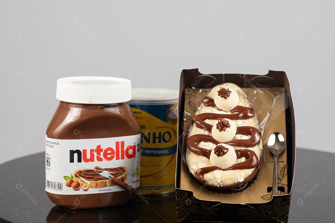 Ovo de páscoa de colher ao lado de leite ninho e nutella sobre uma mesa