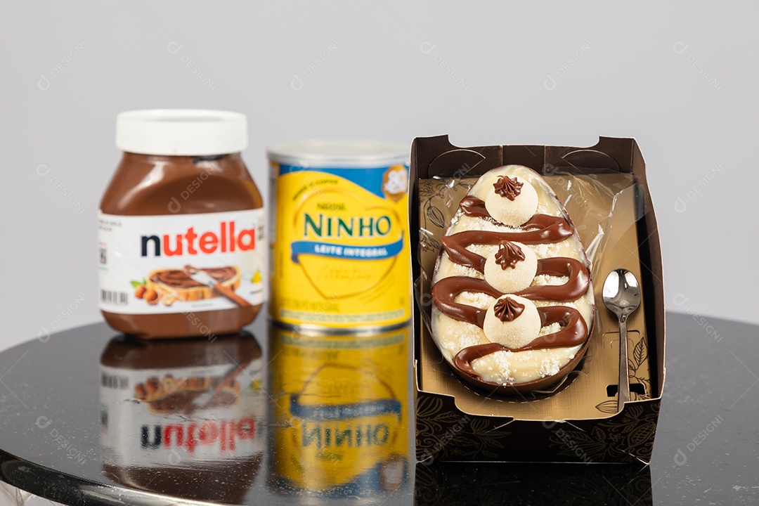 Ovo de páscoa de colher ao lado de leite ninho e nutella sobre uma mesa