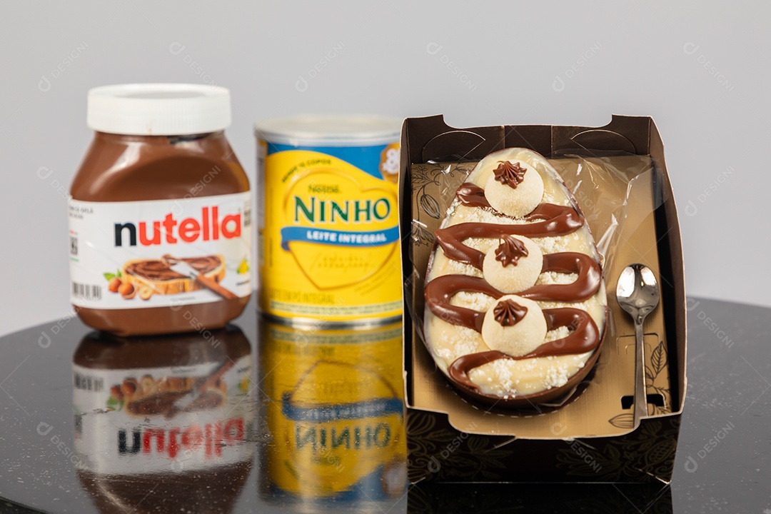 Ovo de páscoa de colher ao lado de leite ninho e nutella sobre uma mesa